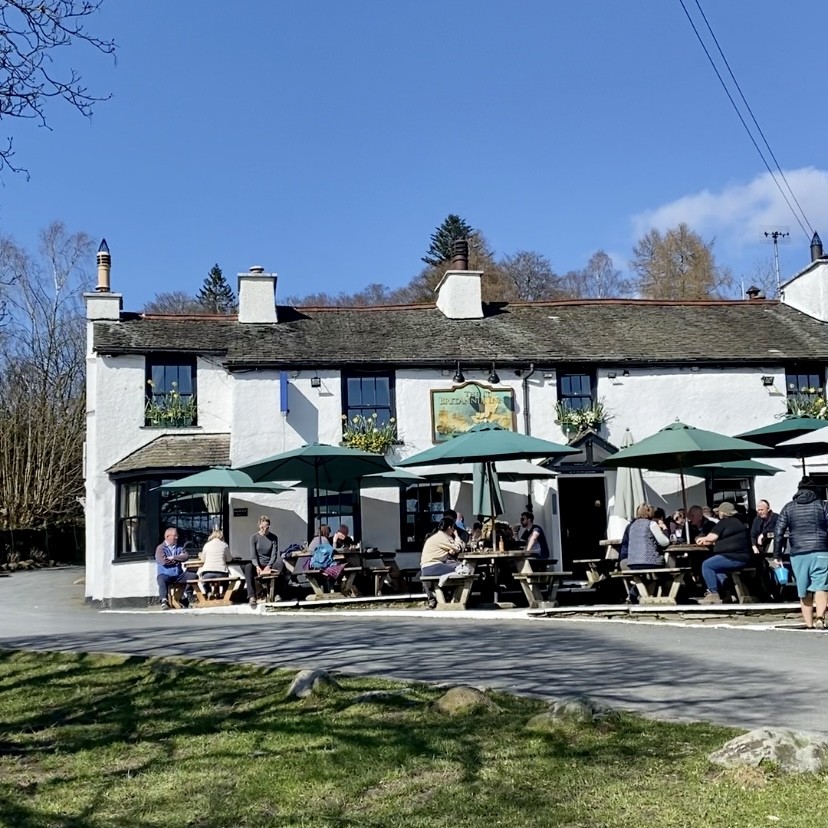 The Britannia Inn in Elterwater with people sitting outside on wooden tables on a sunny day.