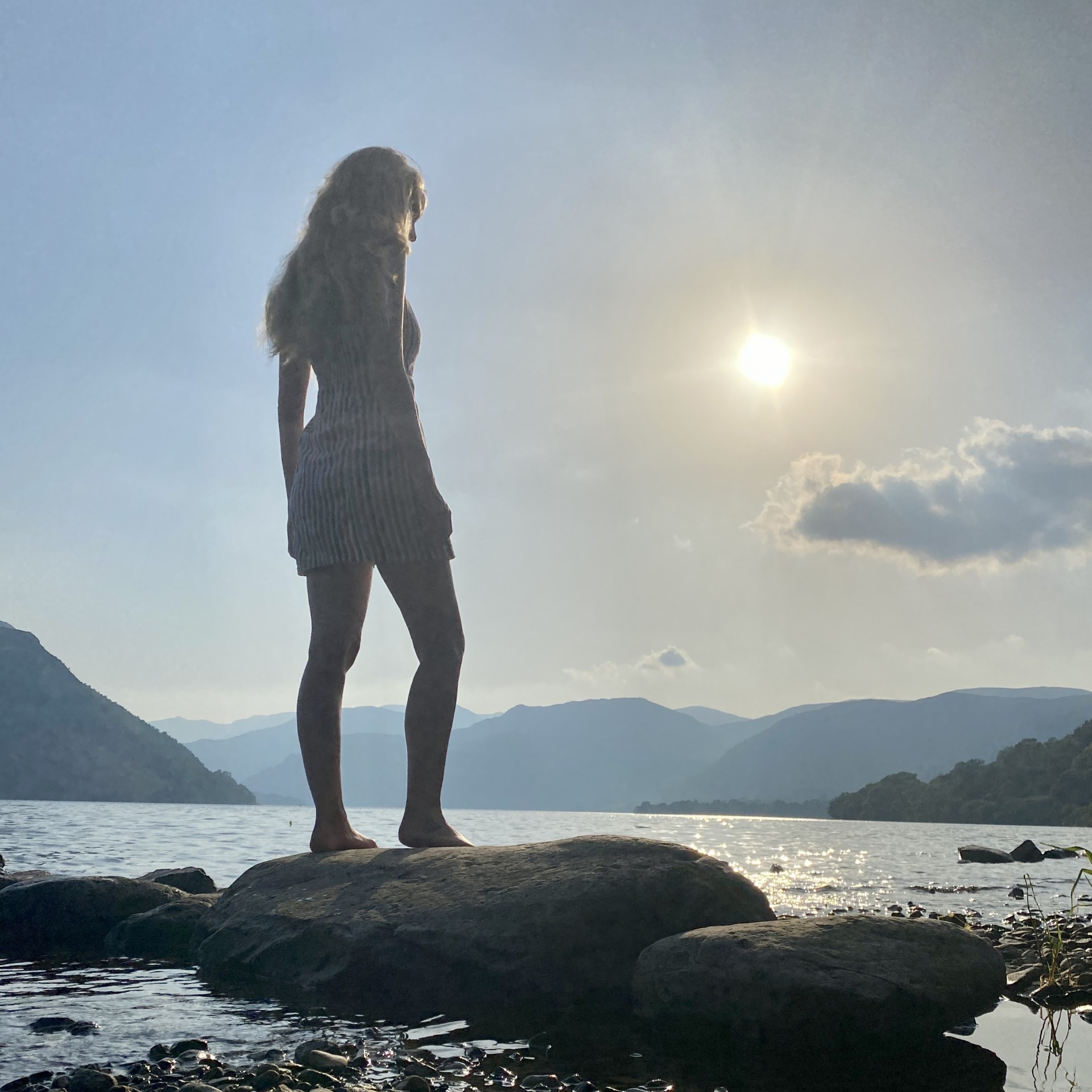A woman standing on a rock by a lake. The weather is sunny and clear.