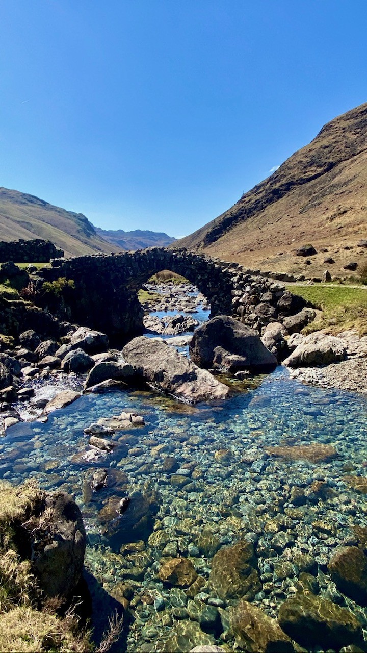 A stone bridge over clear blue water at Esk Falls in The Lake District.