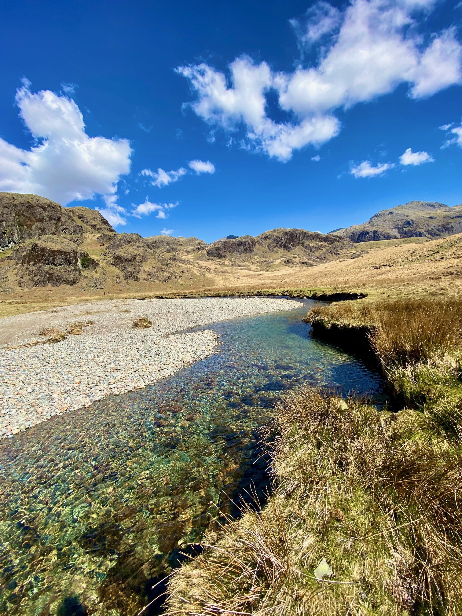 A clear water stream with a pebble beach and mountains in the background in Eskdale, The Lake District.