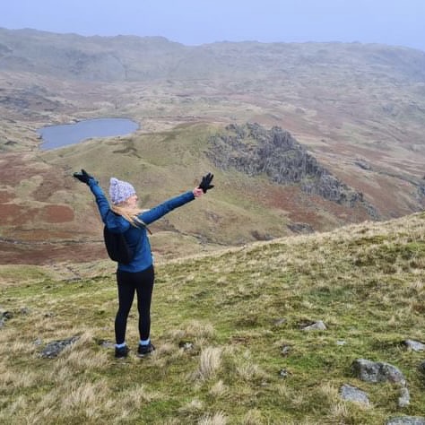A woman up a Lake District fell with her arms up.