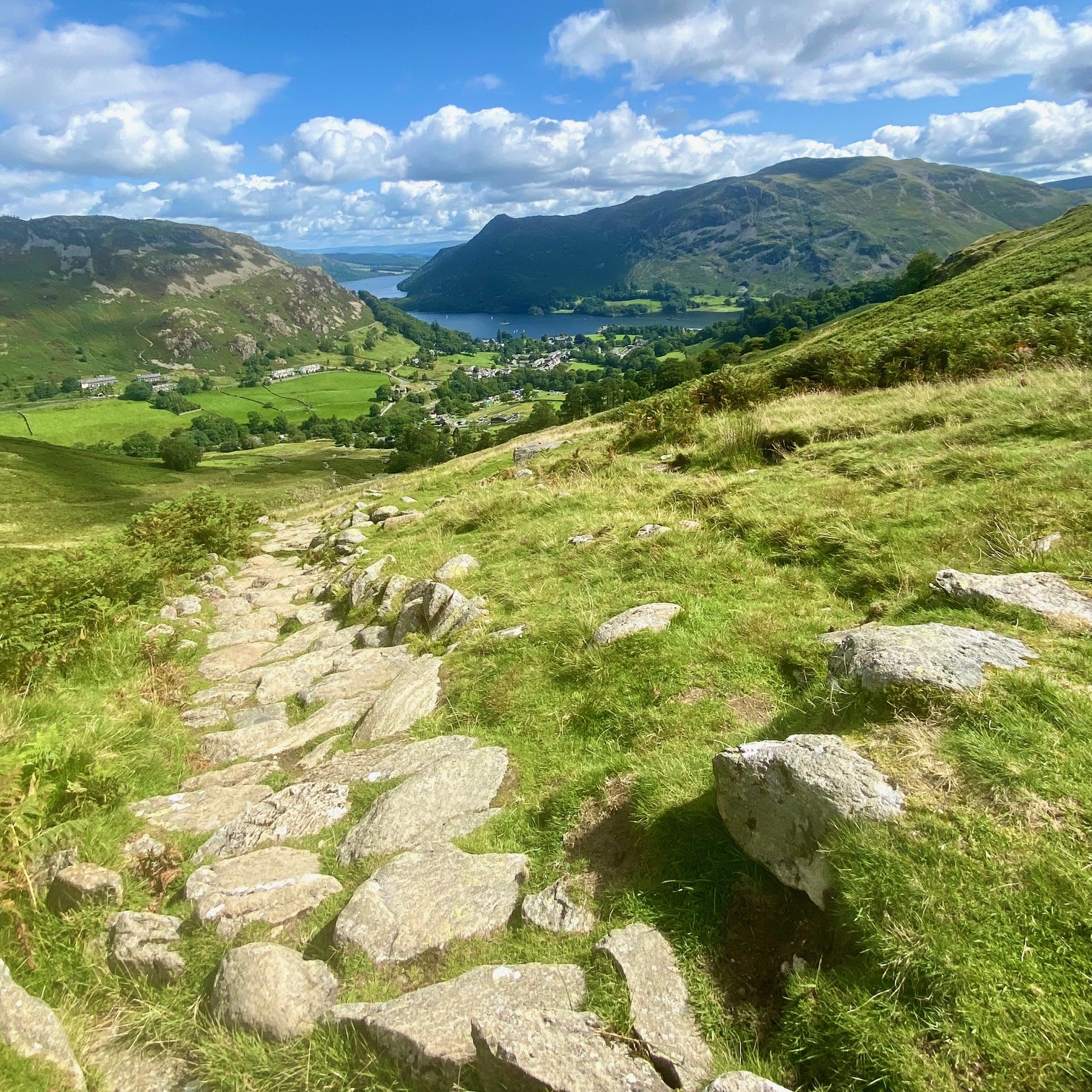 A paved path up a mountain overlooking Ullswater and Glenridding below.