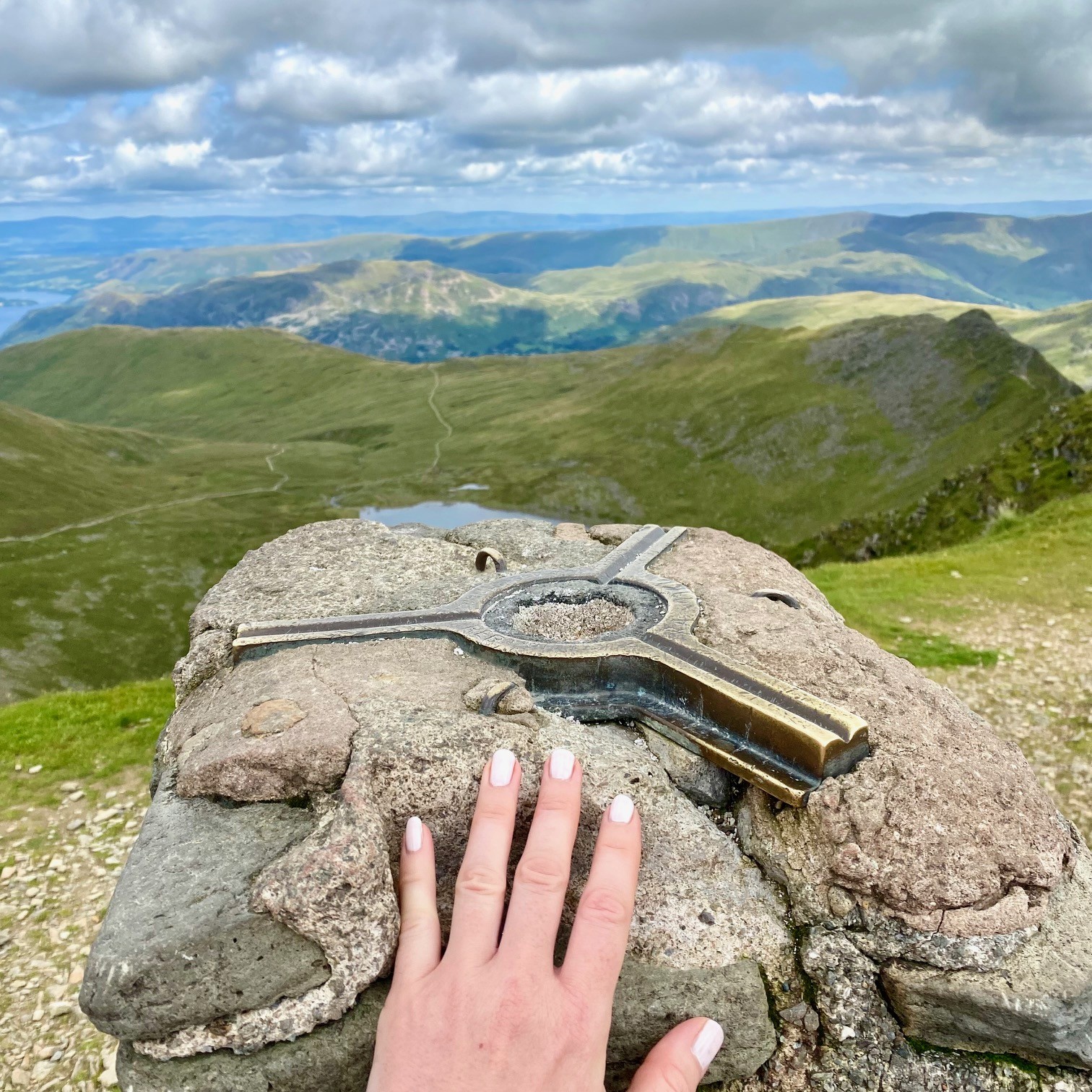 A woman's hand touching the trig point on the summit of Helvellyn.
