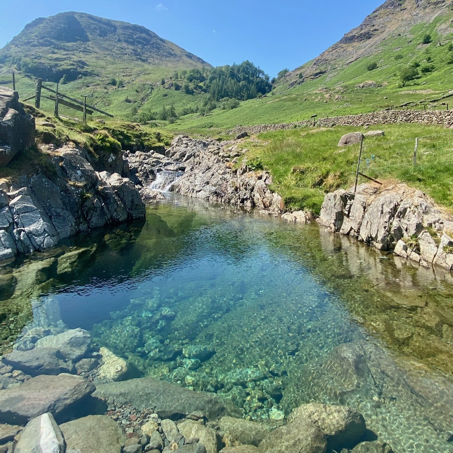 A mountain pool with turquoise water and mountains in the distance, summer in the Lake District.