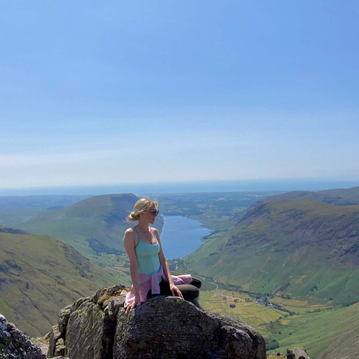 A woman sitting on a rock on a mountain with the view of Wastwater Lake behind her, summer in the Lake District