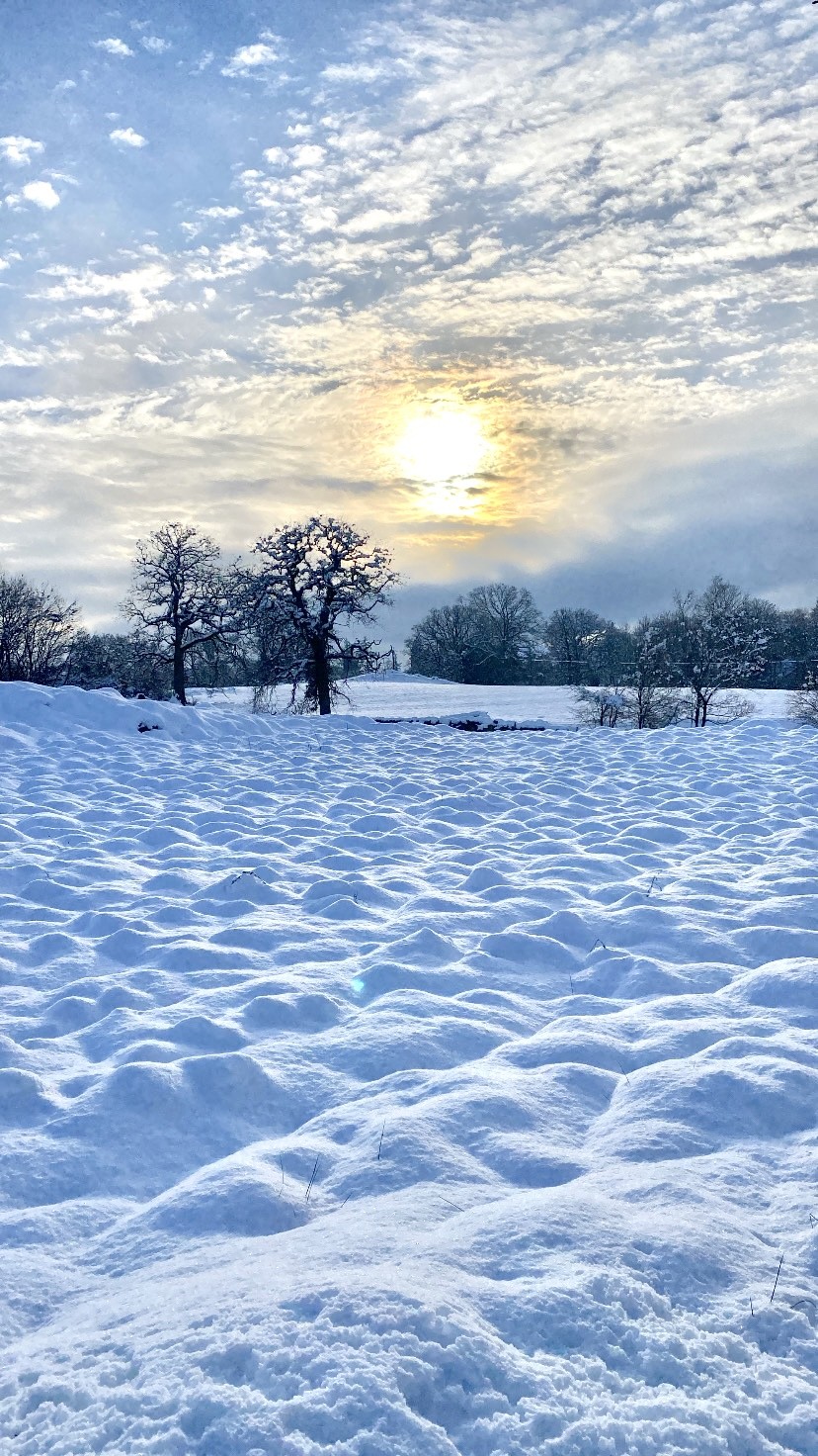 A snow covered field with the sun shining through clouds in the distance. Winter in the Lake District