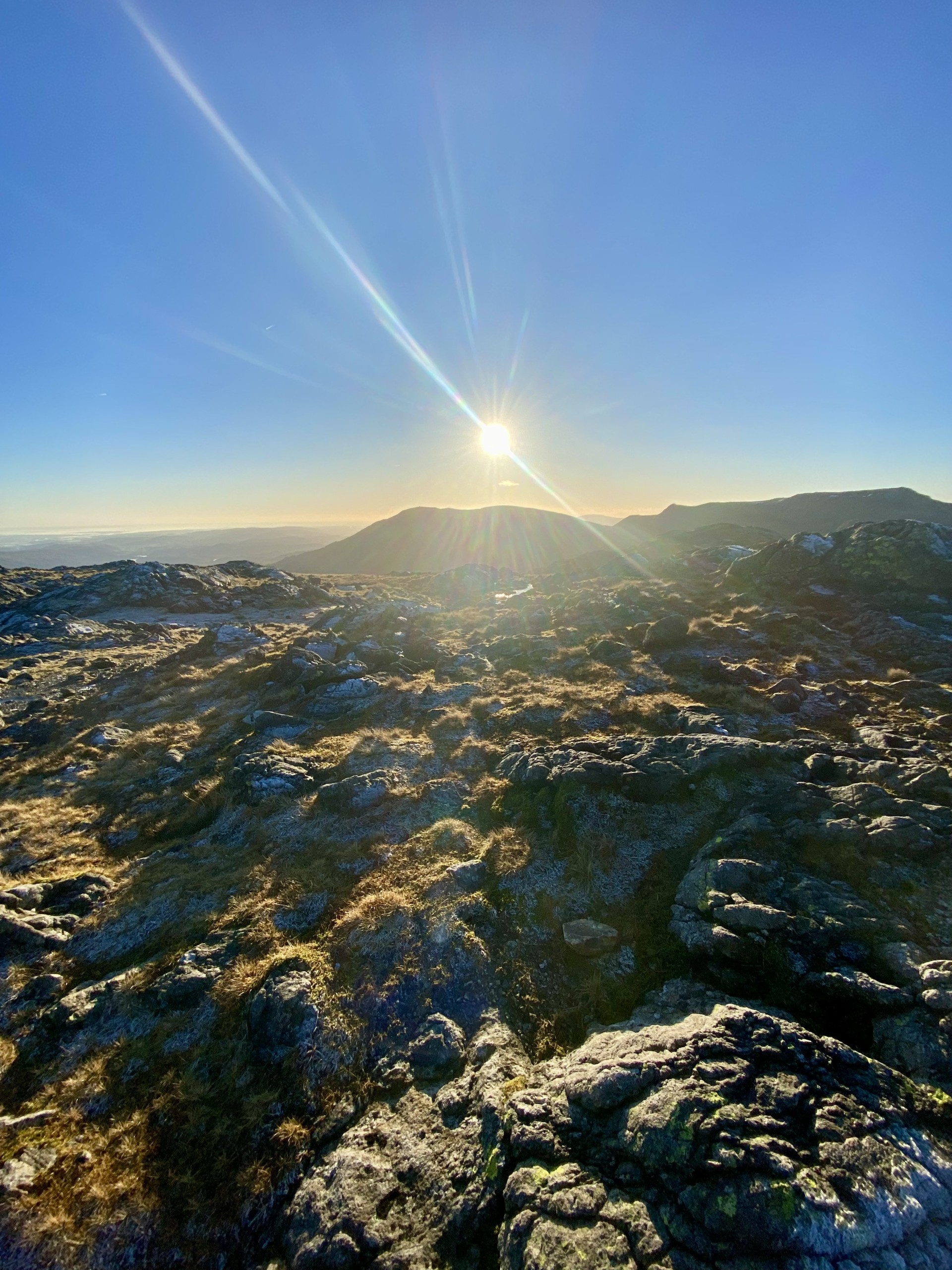 A mountain summit with the sun shining in the distance on a clear day. Winter in the Lake District