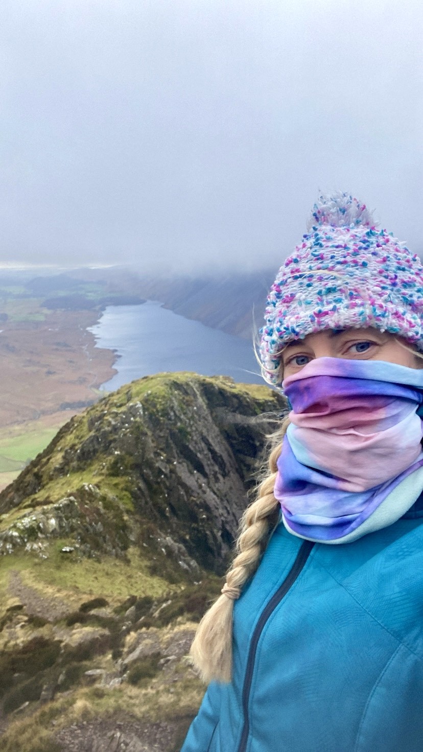 A woman standing in front of the camera up a mountain with a view of Wastwater Lake behind her. Winter in the Lake District