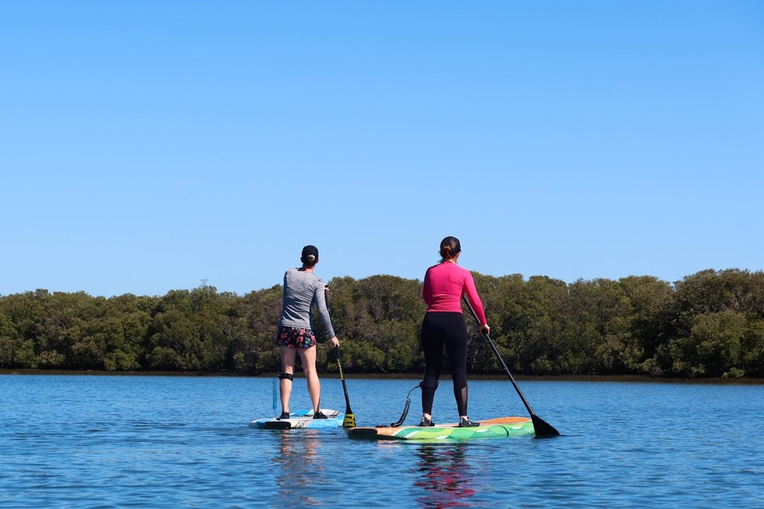 Two women stand up paddleboarding on a lake