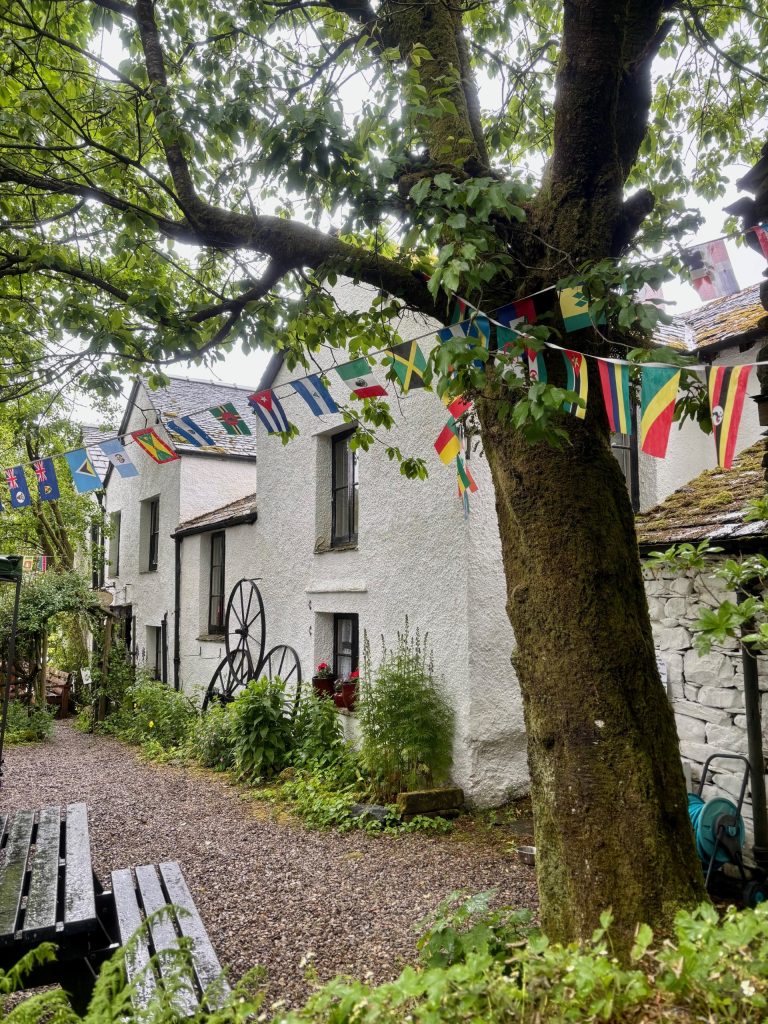 The white farm building of Caffle House Tearooms, in Watendlath. Decorated with flags from countries around the world.